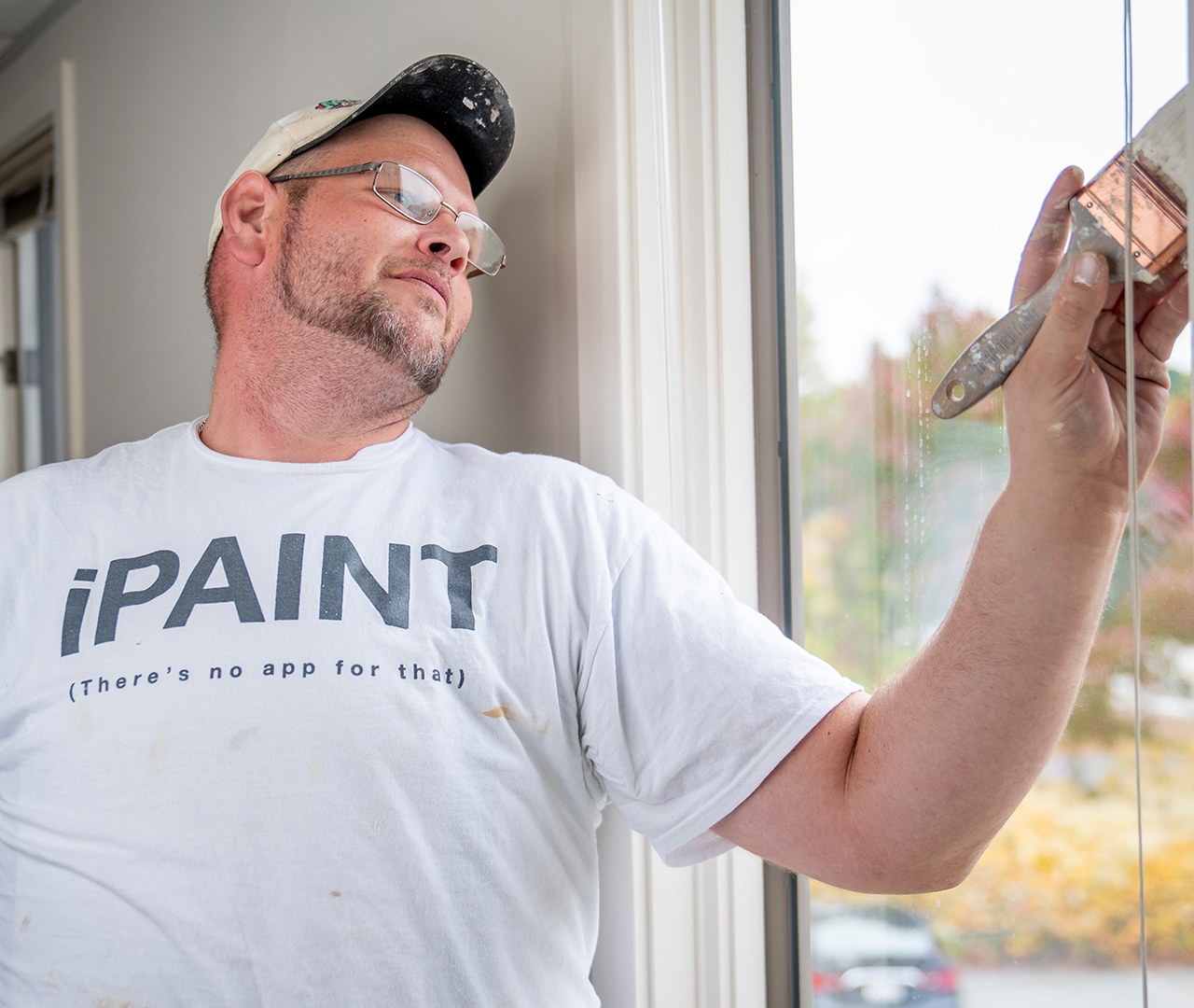 A Castle Complements painter in an iPAINT shirt painting window trim