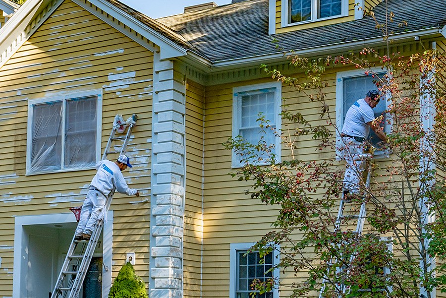 Two painters on ladders painting the upper story of a house