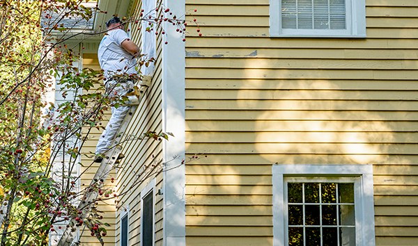A painter on a ladder working on a home's exterior