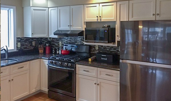 A finished kitchen with white cabinets and stainless appliances