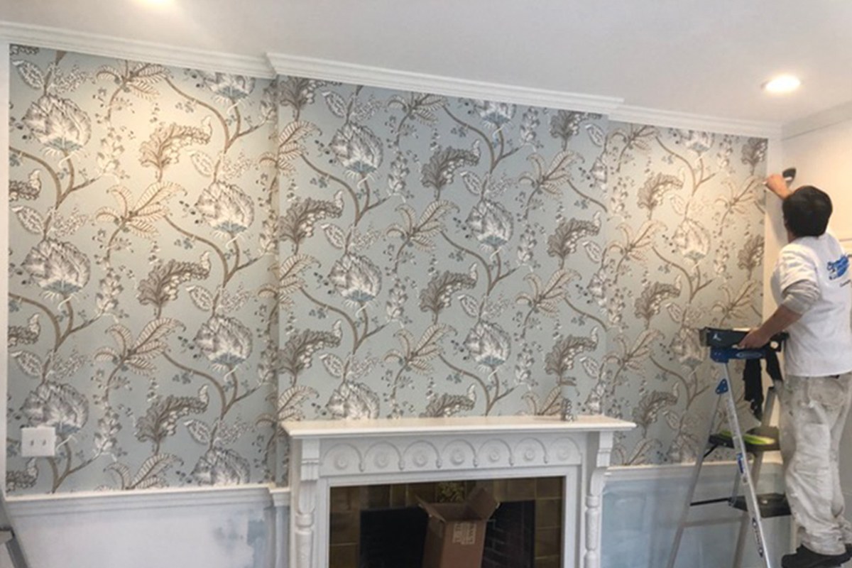 A painter installing patterned wallpaper above a fireplace